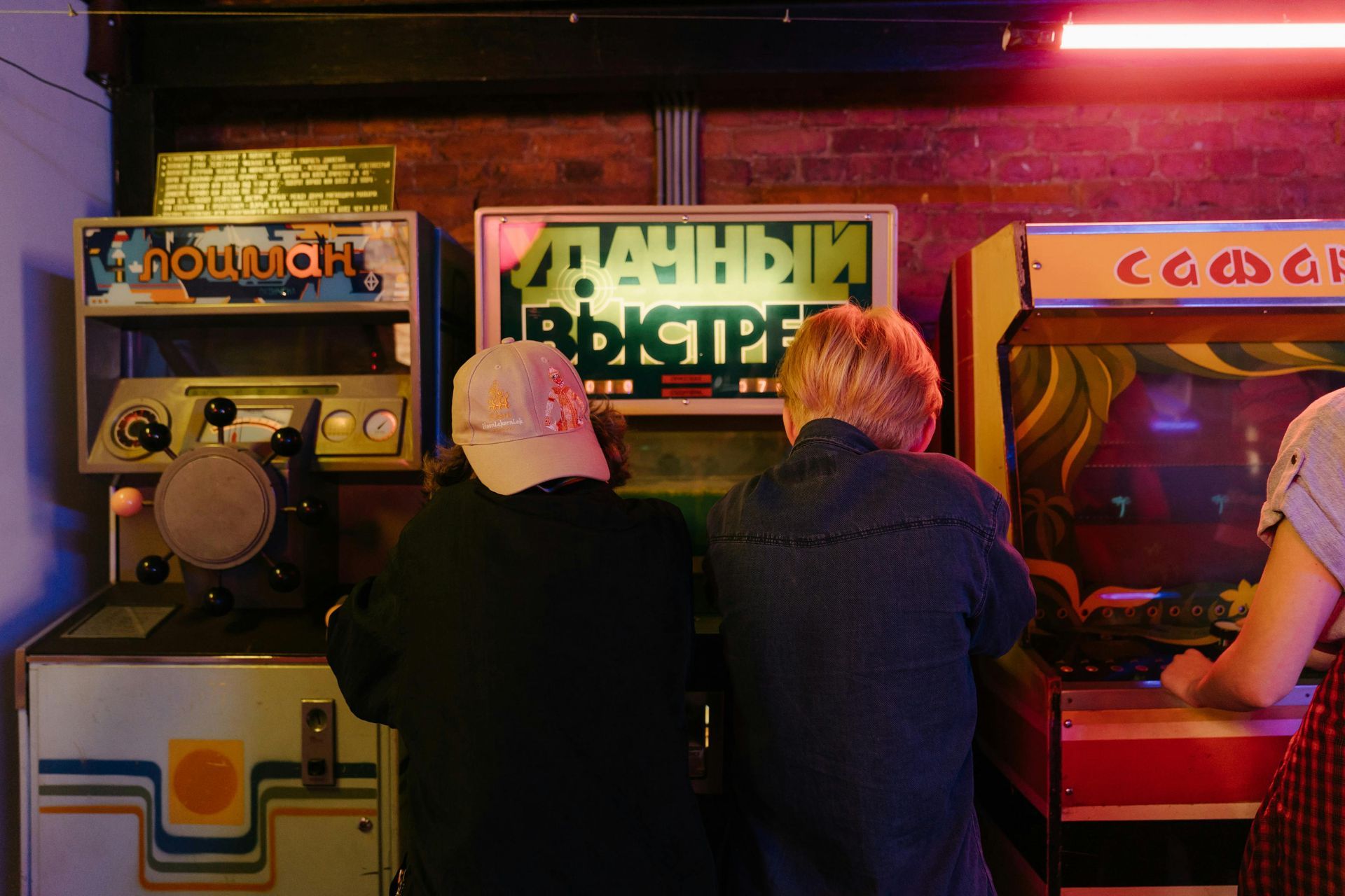 People playing arcade games in a dimly lit arcade with colorful cabinet screens