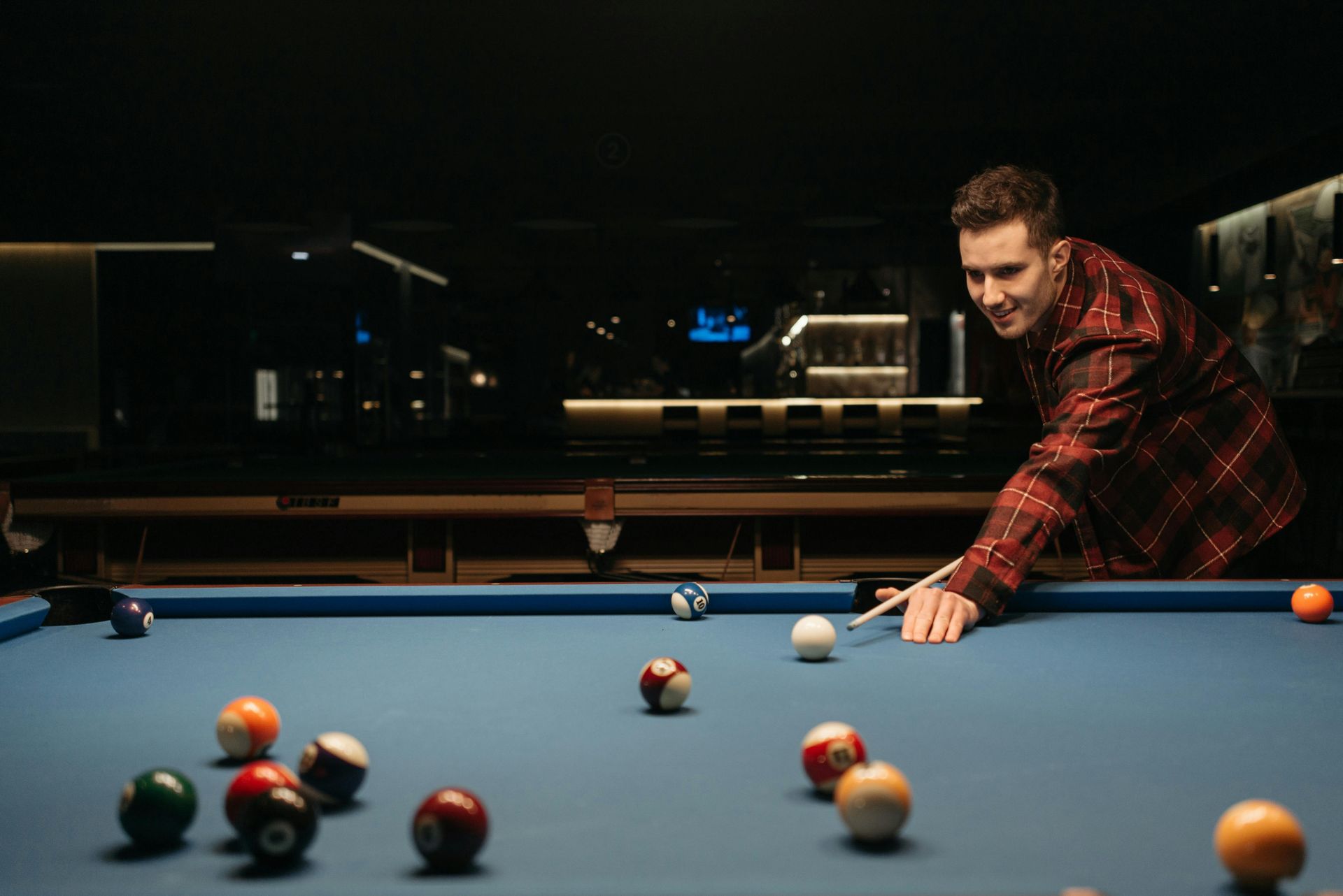 Man lining up a pool shot on a blue billiards table in a dimly lit room