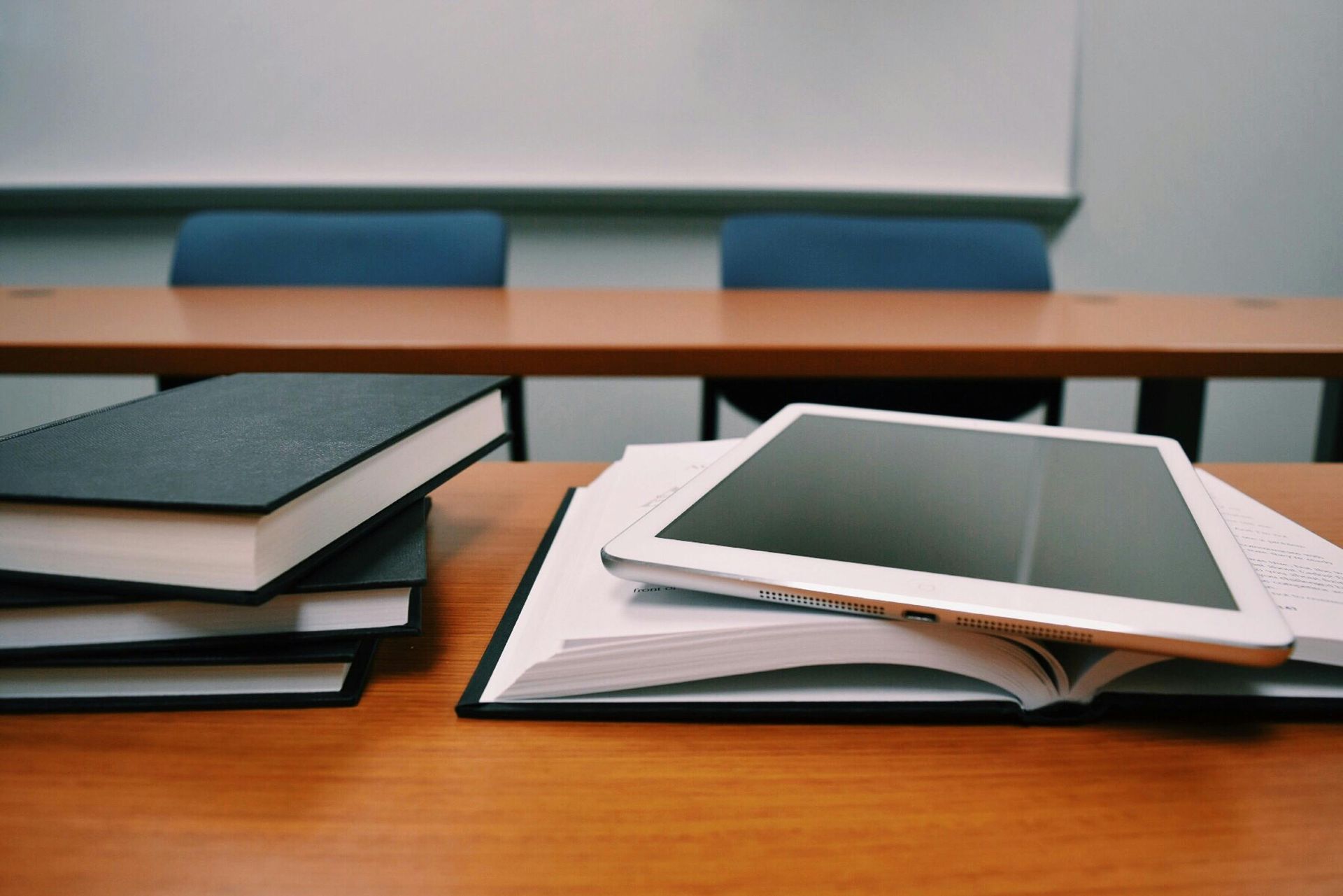 Books and a tablet on a wooden desk in a classroom or study room